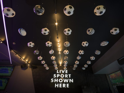 Ceiling hung with rows of footballs and rugby balls, above an illuminated sign reading 