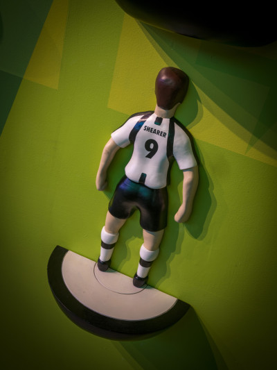 Close-up of a giant Subbuteo-style figure on a green wall, wearing a black and white striped shirt with 